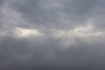 ​A close-up shot capturing a moody, grey sky entirely covered by layered, rain-bearing clouds, featuring a small pale white gap of light.