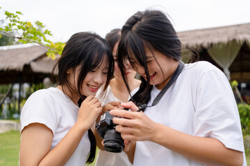 Three teenage friends reviewing photos on a camera outdoors. Real friendship, creativity, and joyful learning captured in a natural park setting.