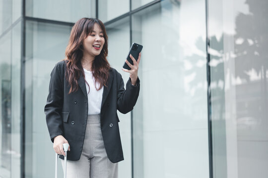 A confident businesswoman walking outside a modern office building while using her smartphone, representing business mobility, communication, and a professional corporate lifestyle.