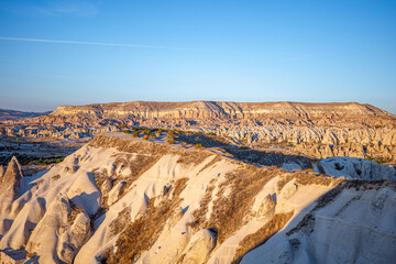 A breathtaking panoramic view of Cappadocia&rsquo;s iconic rock formations glowing under the warm golden light of sunset in Turkey. The soft sandstone valleys, rugged ridges, and layered textures