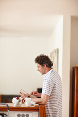 Tablet, reading and man in kitchen in home with online blog, email or notification of communication. Coffee, contact and male person with digital technology for connectivity on app in apartment.