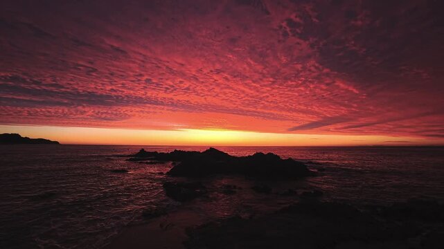 Pre-sunrise red cloud streaks over rocky shoreline Spain in warm twilight