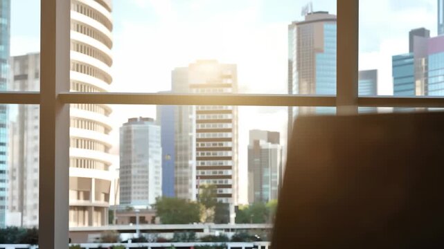 A sleek laptop sits atop a wooden table with stacks of newspapers scattered around. They are illuminated by warm light from a sunset, highlighting a bustling urban backdrop.