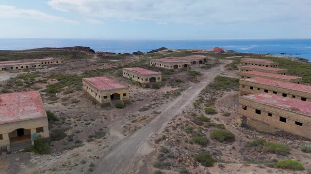 Aerial drone view flying along the derelict rows of residential blocks within the abandoned Abades Leper Colony and Sanatorium ruins in Tenerife, Canary Islands, Spain.