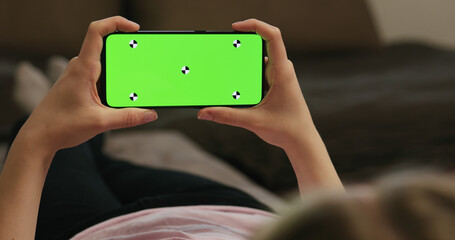 young woman lying on a couch and holding smartphone with horizontal green screen