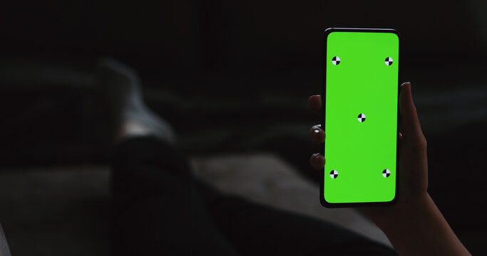 young woman lying on a couch and holding smartphone with vertical green screen