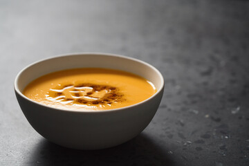 Pumpkin soup decorated with herbs and olive oil in white bowl on concrete background with copy space