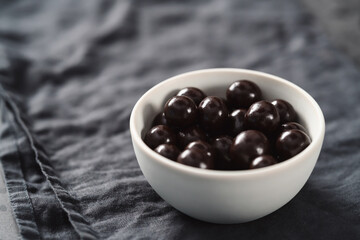 Chocolate drage with hazelnuts nuts in white bowl on linen background