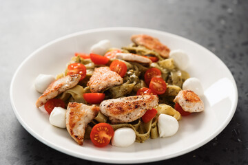 fettuccine with pesto, tomatoes , mozzarella and chicken on white plate