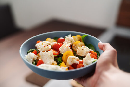 amn hand hold salad with red and yellow cherry tomatoes , mozzarella and spinach in blue bowl
