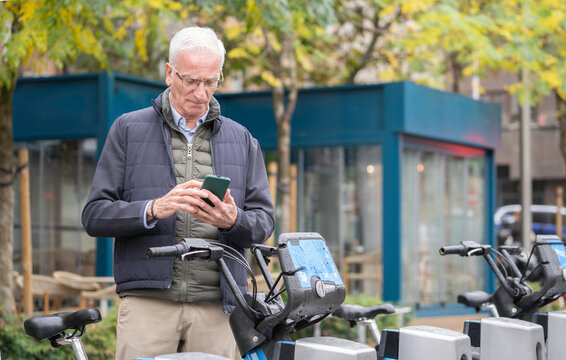 Senior man checking his smartphone for an urban bike share rental in the city with copy space - Powered by Adobe