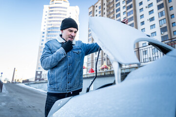 Worker examines engine on frosty street, Individual inspects frozen vehicle engine in winter...
