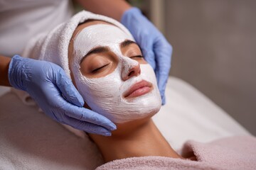 Relaxing facial treatment at a spa with a mask applied to a client's face while a professional attends to her skin