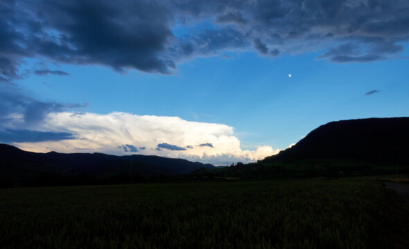 Huge white storm cloud moves over the Swabian alb. In the foreground the silhouette of trees and fields is visible, beautiful blue sky. Germany