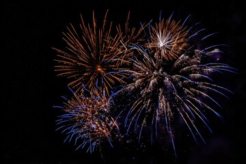 Explosive Burst Of Fireworks Illuminated Against A Black Night Sky Displaying Golden And Blue Sparks