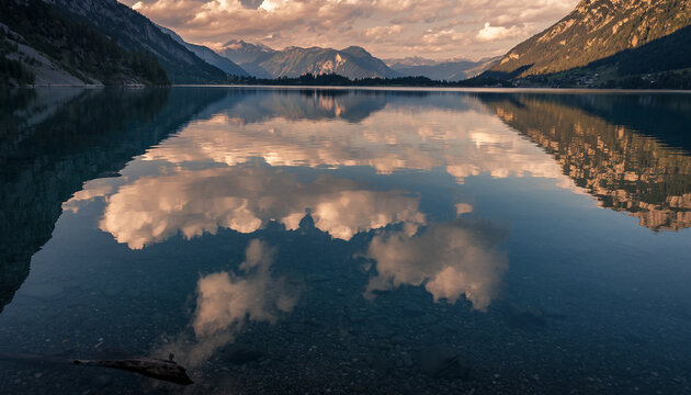 A tranquil mountain lake perfectly reflecting the cloudy sky and distant peaks, showcasing clear water and serene natural beauty.