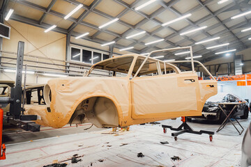 Specialist spraying anti rust sealant into the hidden chassis cavities. Protection against corrosion and internal body element sealing in a professional auto service shop