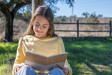 Young girl enjoying a peaceful moment outdoors, leaning against a wooden post and deeply immersed...