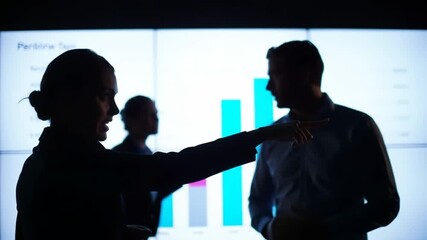 Silhouetted team of business professionals in a dark office collaborating on a presentation, analyzing data charts on a large screen - Powered by Adobe