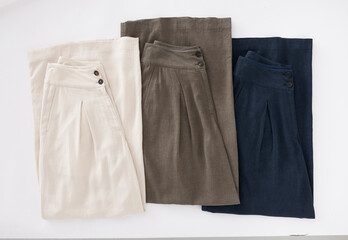 Three pairs of stylish linen trousers in neutral colors on white background