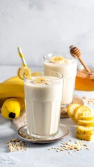 Two banana smoothies garnished, ingredients nearby, neutral background