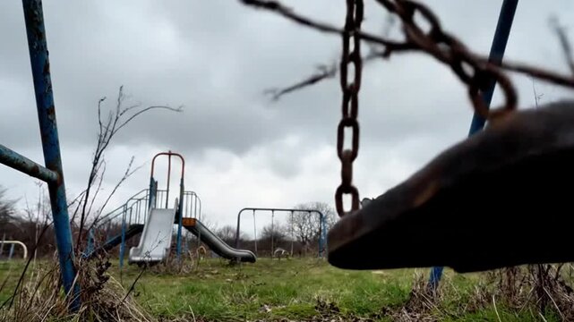 A child&rsquo;s swing moving slowly in the wind on an empty playground, overcast sky, abandoned feeling, emotional.