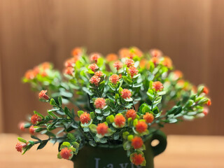 A vibrant close-up shot of a cluster of small artificial flowers with bright reddish-orange or salmon-pink blossoms and lush green plastic leaves.