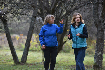 Mother and young adult daughter talking and gesturing while walking outdoors in autumn