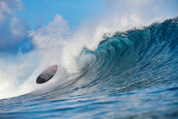 Surfboard thrown by towering blue wave, board flipping midair with frothy spray and curling barrel at dawn light