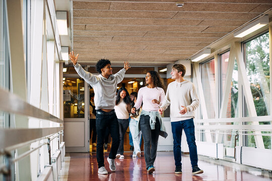 Teenage boy with arms outstretched enjoying while walking near friends in school corridor
