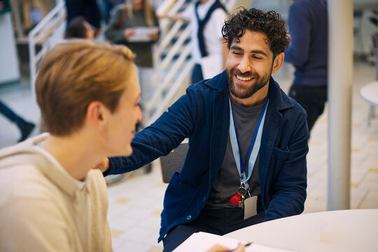 Smiling male teacher talking with student while sitting in school lobby
