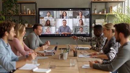 A diverse group of colleagues participates in a video conference meeting in a modern office setting. - Powered by Adobe