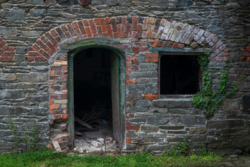 The wall of an abandoned, industrial building shows crumbling stone and brick, flanked by climbing ivy. Photo taken in Inniskeen, County Monaghan, Ireland 