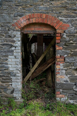 Detail of a green-painted wooden door slightly ajar in a stone wall with brick surround, revealing shadows, debris. Photo taken in Inniskeen, County Monaghan, Ireland