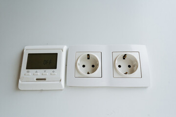 thermostat on wall, digital thermostat with controls, electronic thermostat installed next to power outlets, white digital thermostat mounted on neutralcolored wall for energy