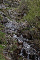 Waterfall of Chorrera de Mojonavalle, Canencia, Madrid, Spain, flowing over mossy rocks and surrounded by lush spring vegetation in a peaceful mountain forest setting