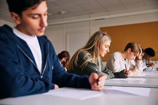 Focused blond girl writing educational exam while sitting at desk in high school classroom