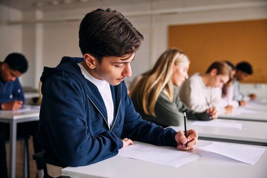 Focused teenage male student writing educational exam while sitting at desk in high school classroom