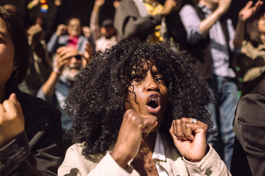 Mature woman with curly hair cheering at game in stadium stand on sunny day