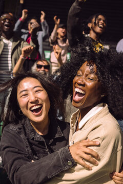 Carefree female friends screaming while celebrating in stadium stand on game day