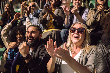 Happy male and female supporters enjoying game from sports stadium stand