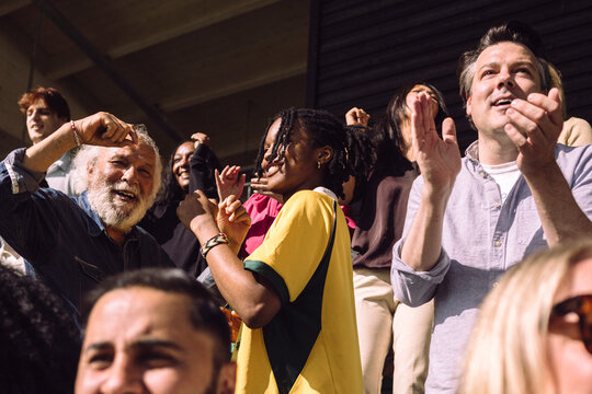 Carefree male supporters dancing while enjoying game from stadium stand on sunny day
