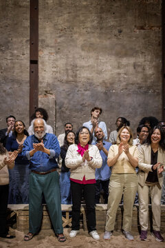 Full length of happy senior male and female spectators giving standing ovation with audience at stage theater