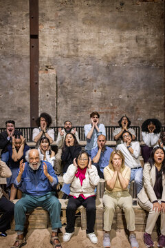 Shocked audience with different facial expressions sitting in theater stand while watching stage play