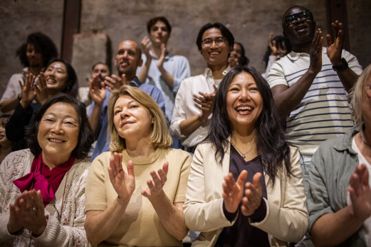 Happy women clapping while watching play in theater