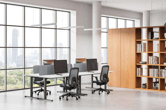 Fototapeta Modern open space office interior with workstations, ergonomic chairs, large windows, and wooden bookshelf in bright daylight setting. 3D Rendering