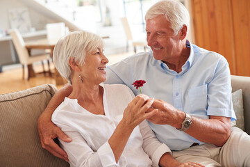 Love, happy or old couple on sofa with flower, bonding gift or connection in retirement. Smile, mature man or woman in house with healthy relationship, commitment or floral present in nursing home.
