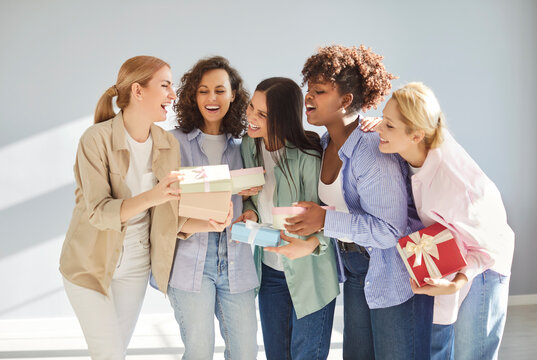 Group of cheerful multiracial women exchanging wrapped gift boxes, laughing and celebrating special ocasion together. Happy female friends holding presents on birthday or International Women Day.