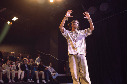 Young male keynote speaker with braided hair gesturing while explaining in seminar at theater