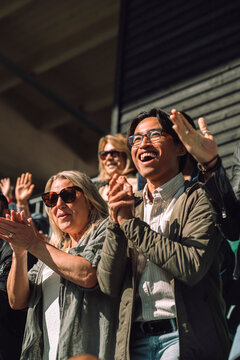 Happy male and female sports fan clapping and cheering while standing in stadium stand